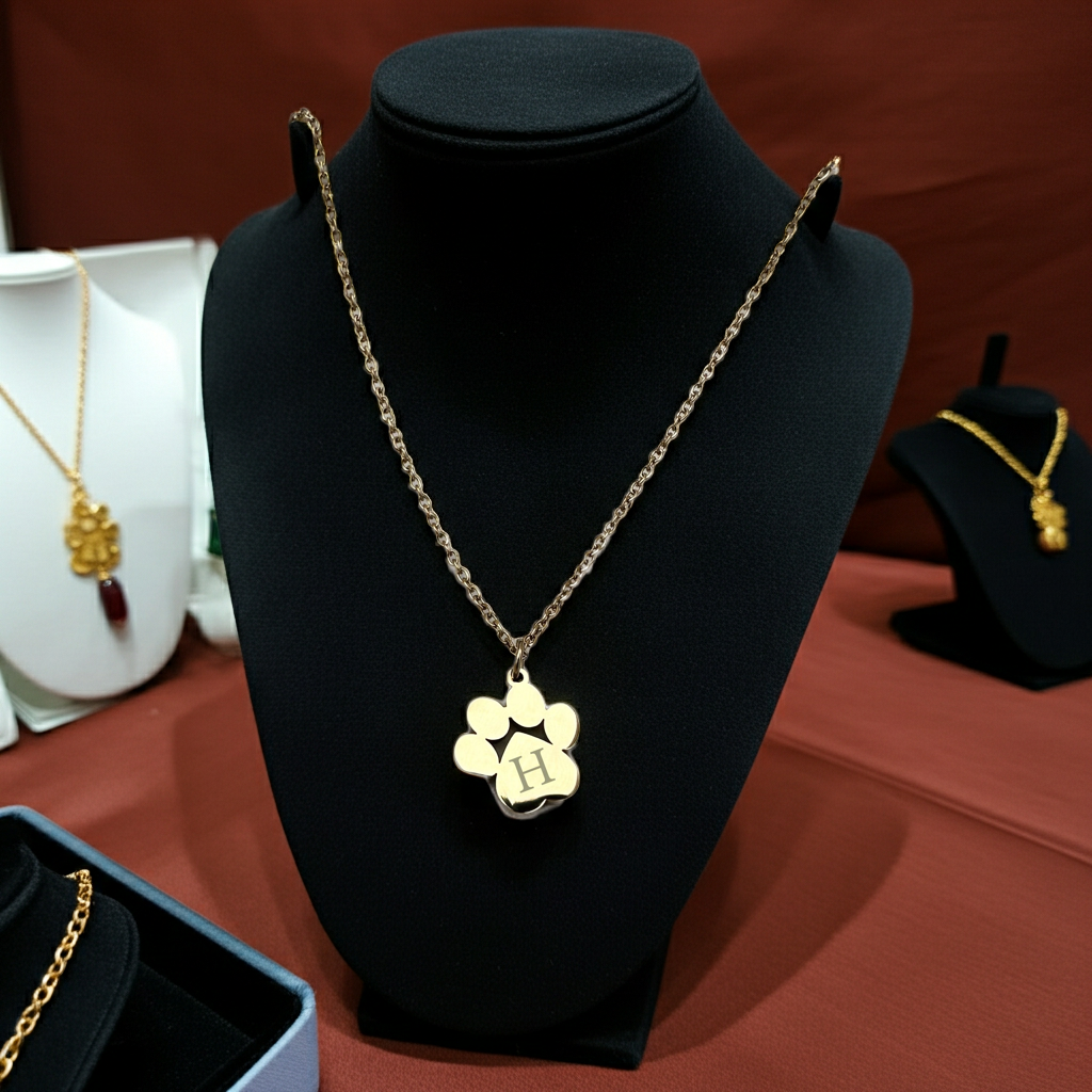 Gold necklace with a paw-shaped pendant on a black stand against a brown background